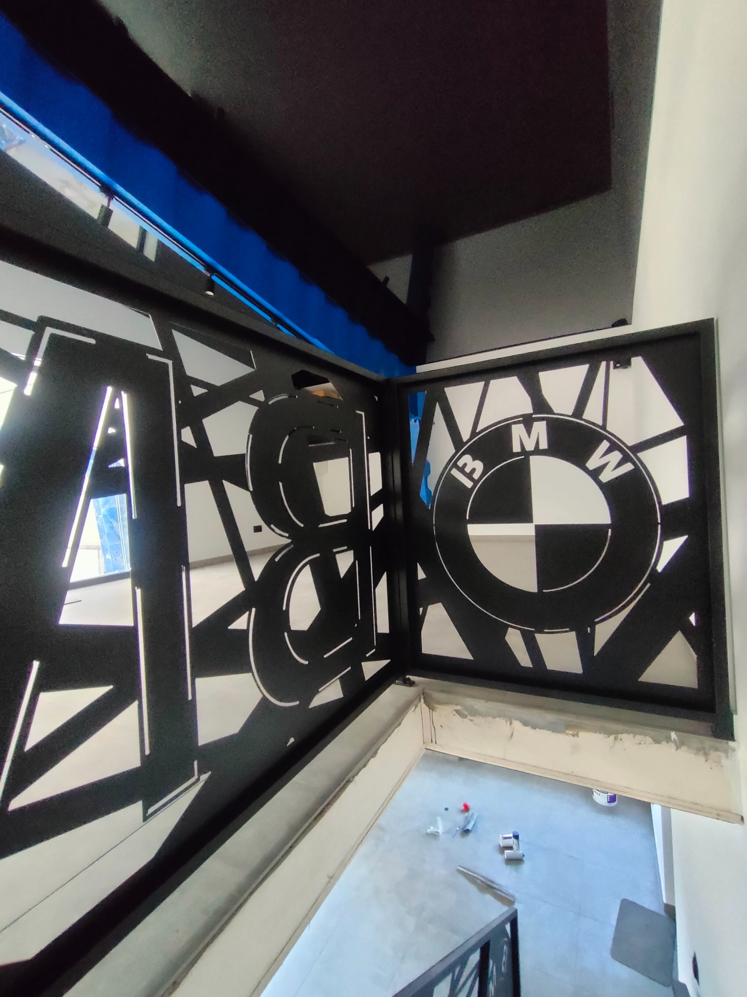 Czarna, metalowa balustrada schodowa z wyciętymi laserowo wzorami geometrycznymi i logo BMW, widok z góry na schody w trakcie wykończenia.