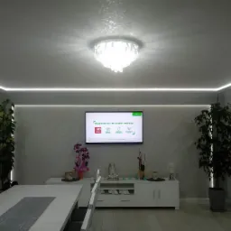 Jasne wnętrze jadalni z dekoracyjną lampą sufitową, podświetleniem LED i ścianą w odcieniach szarości o nieregularnej fakturze.