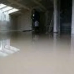 Błyszcząca, mokra powierzchnia świeżo wylanej posadzki w pomieszczeniu z oknami dachowymi, widoczna postać osoby w tle.