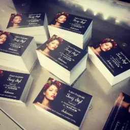 Stosy wizytówek salonu fryzjerskiego i solarium 'Twój Styl' z wizerunkiem kobiety z wiankiem na głowie, ułożone na metalowej powierzchni.