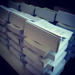 Stosy świeżo wydrukowanych, białych arkuszy papieru z widocznym tekstem, ułożone w równe stosy, czekające na dalszą obróbkę introligatorską.