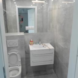 art-bud - Nowoczesna łazienka w odcieniach szarości z podwieszaną szafką umywalkową, wiszącą toaletą i dużym lustrem z widocznym odbiciem pokoju z żyrandolem.