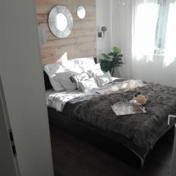 art-bud - Jasna sypialnia z drewnianą ścianą za łóżkiem, ozdobiona trzema okrągłymi lustrami, na łóżku futrzana narzuta i srebrna taca z filiżankami, podłoga z ciemnego drewna.