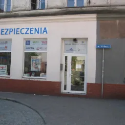 Fasada budynku z napisem 'UBEZPIECZENIA' nad witrynami z logo różnych towarzystw ubezpieczeniowych: Compensa, Uniqa, HDI, Tuz, Warta, Generali oraz wejściem do biura Gothaer Proama Aviva, przy...