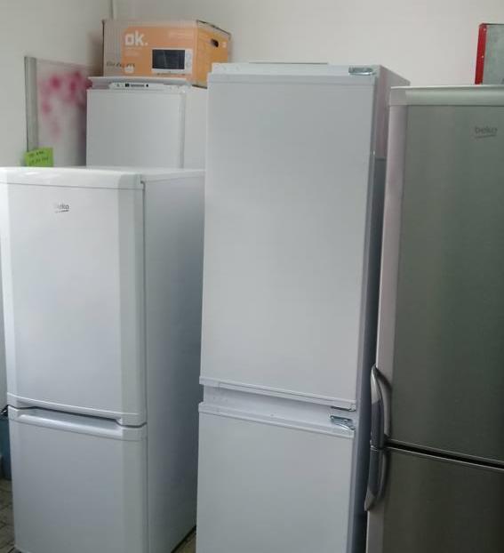 Ustawione obok siebie lodówki różnych producentów (Beko, OK) w magazynie lub sklepie, niektóre z widocznymi uszkodzeniami.