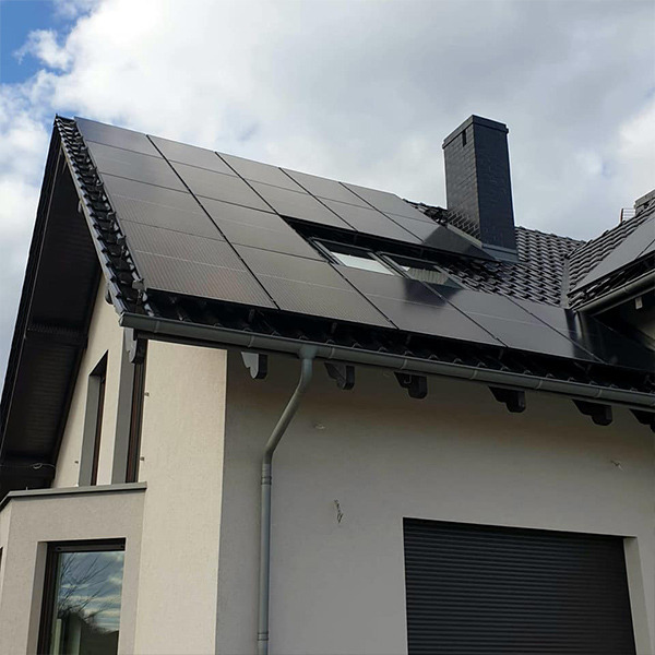 Czarny dach z panelami fotowoltaicznymi na nowoczesnym domu z kominem i oknem dachowym, widok z dołu.