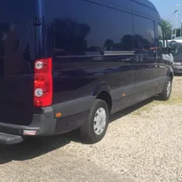 Niebieski samoch&oacute;d dostawczy marki Mercedes-Benz Sprinter zaparkowany na żwirowym parkingu w słoneczny dzień.