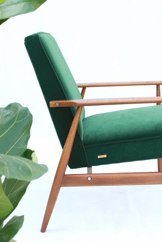 Z bliska widok boczny odnowionego fotela w stylu retro, z zieloną welurową tapicerką i drewnianymi podłokietnikami, z widoczną małą złotą plakietką producenta.