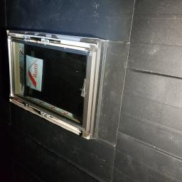 Wooden Houses - Nowe okno dachowe marki Roto, zamontowane w czarnej, drewnianej konstrukcji dachu, z widoczną folią ochronną na szybie.