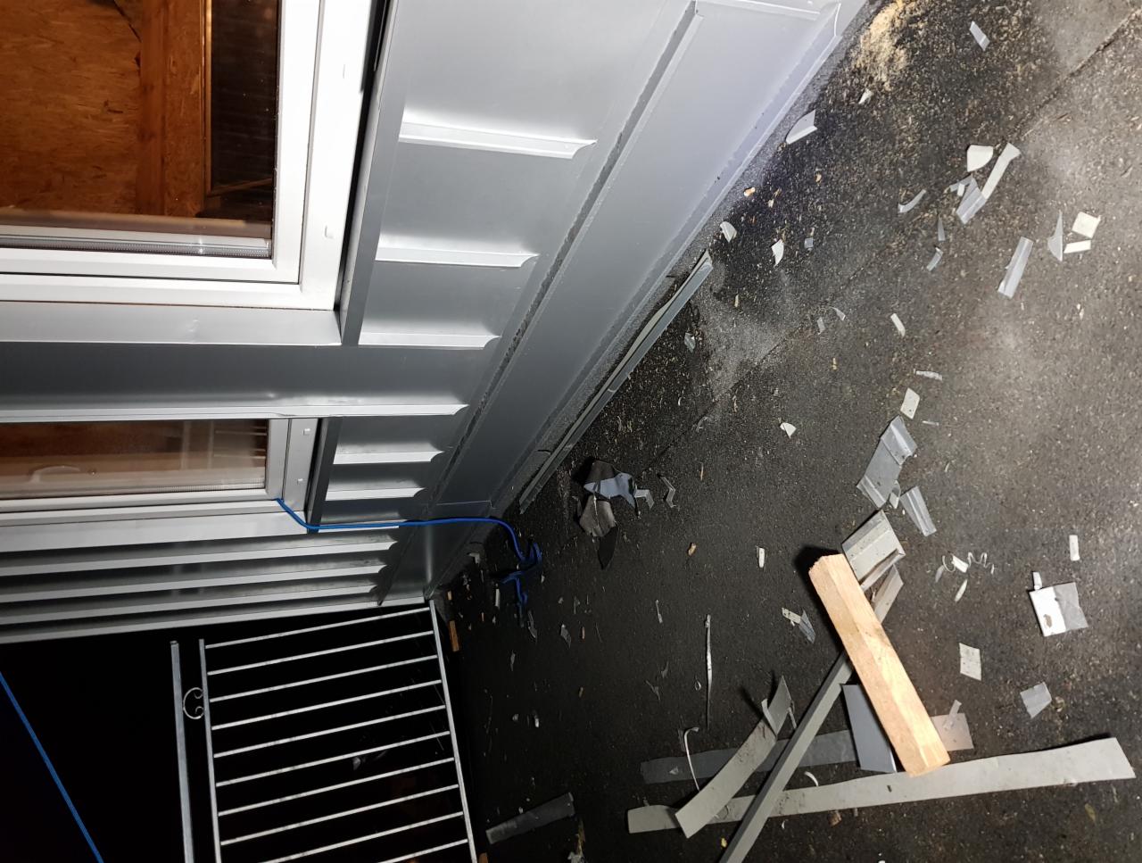 Szare obróbki blacharskie okna po montażu, z widocznymi fragmentami blachy na ziemi i niebieskim przewodem wzdłuż ramy okiennej.