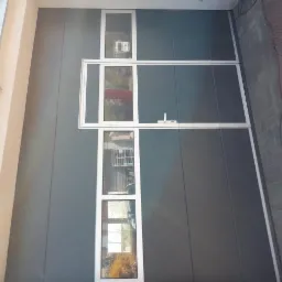 Szara brama przemysłowa z oknami i białymi ramami, widoczna z boku, z oświetleniem zewnętrznym.