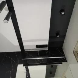 Nowoczesne wnętrze z czarno-białym sufitem podwieszanym, oświetleniem punktowym i paskami LED, oraz ścianą imitującą czarny marmur z białymi żyłami.