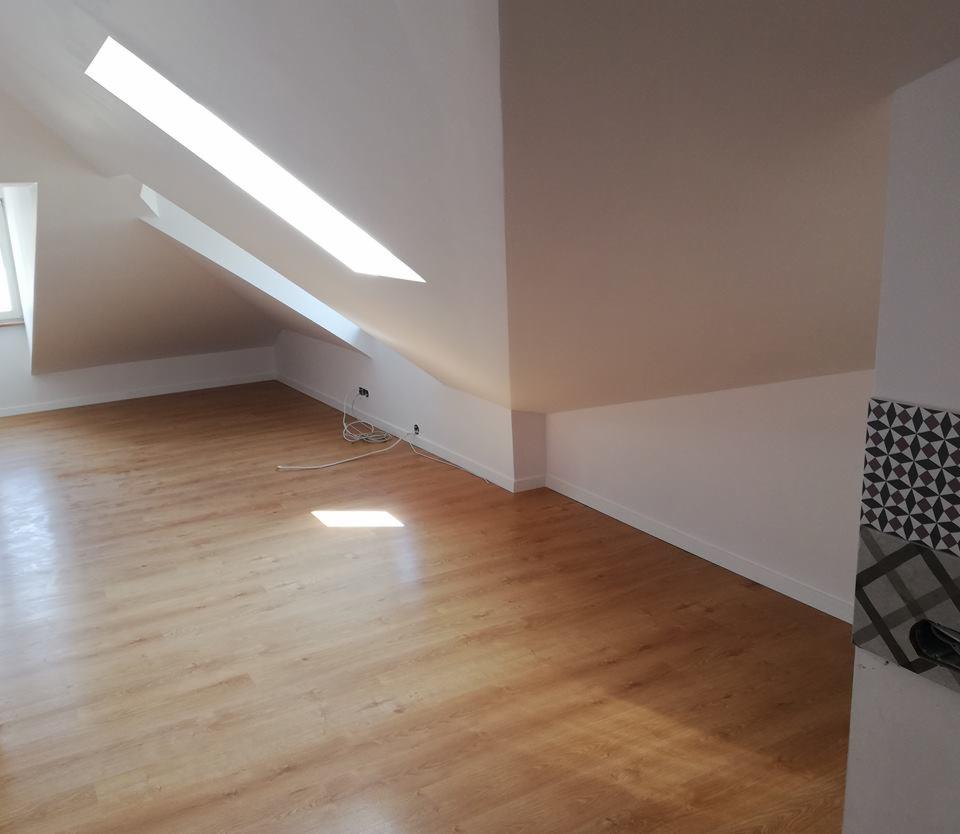Poddasze po remoncie z drewnianą podłogą, świeżo pomalowanymi ścianami i oknami dachowymi wpuszczającymi światło.