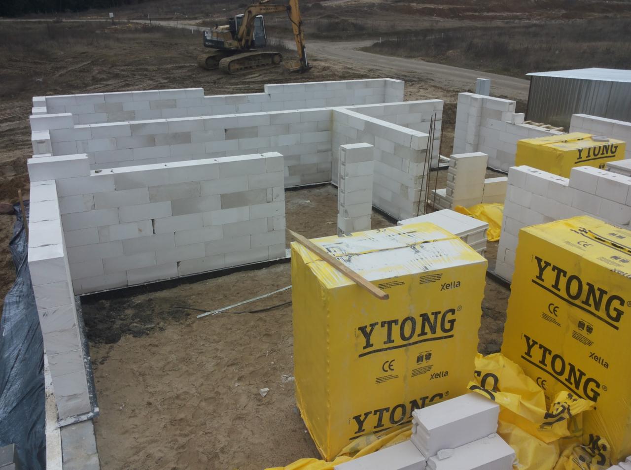 Wznoszenie ścian parteru domu z bloczków Ytong, widoczne palety z bloczkami oraz koparka w tle.