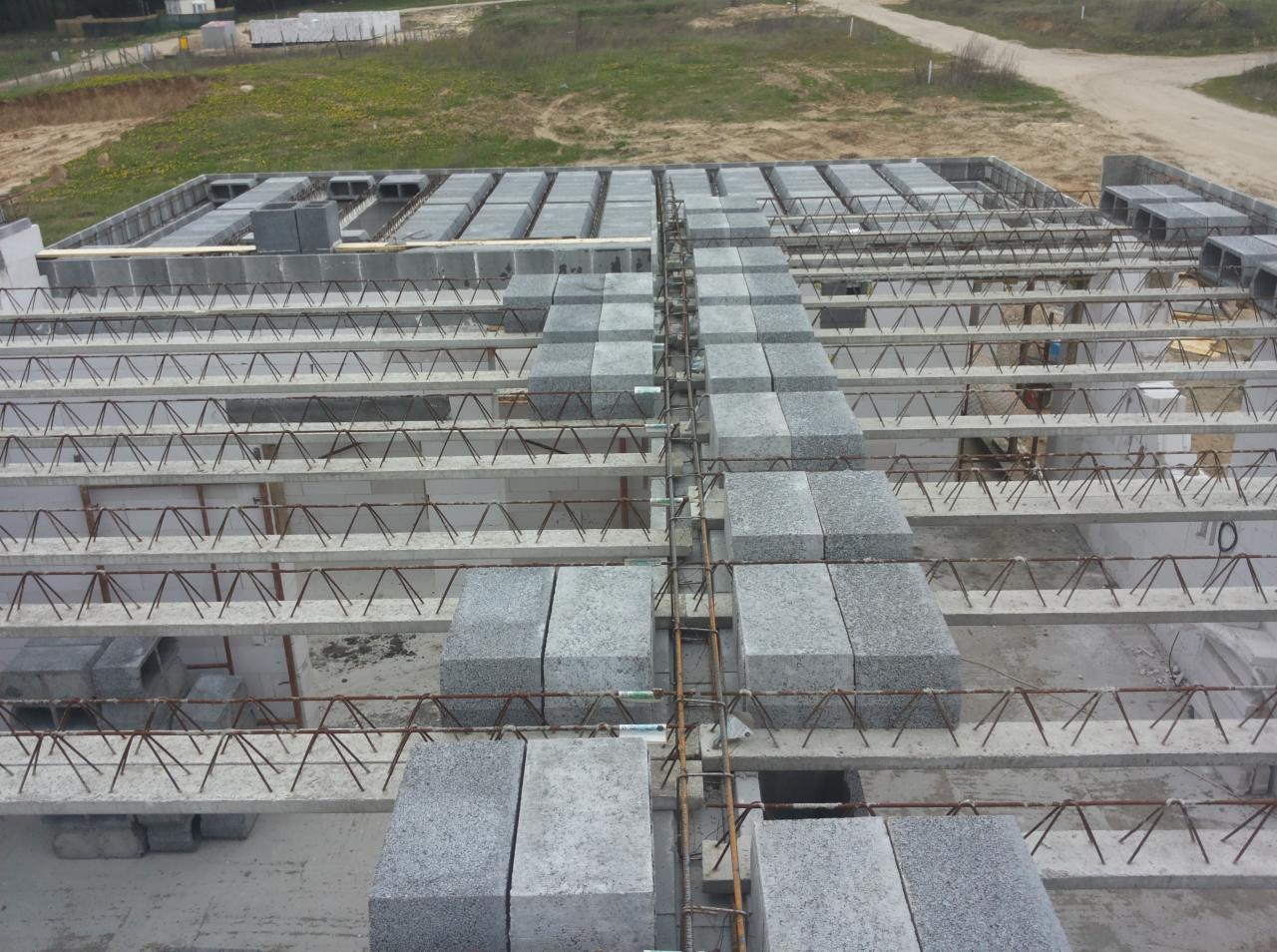 Wczesny etap budowy domu: widok z góry na strop Teriva z betonowymi belkami i pustakami szalunkowymi, zbrojenie ułożone wzdłuż belek.