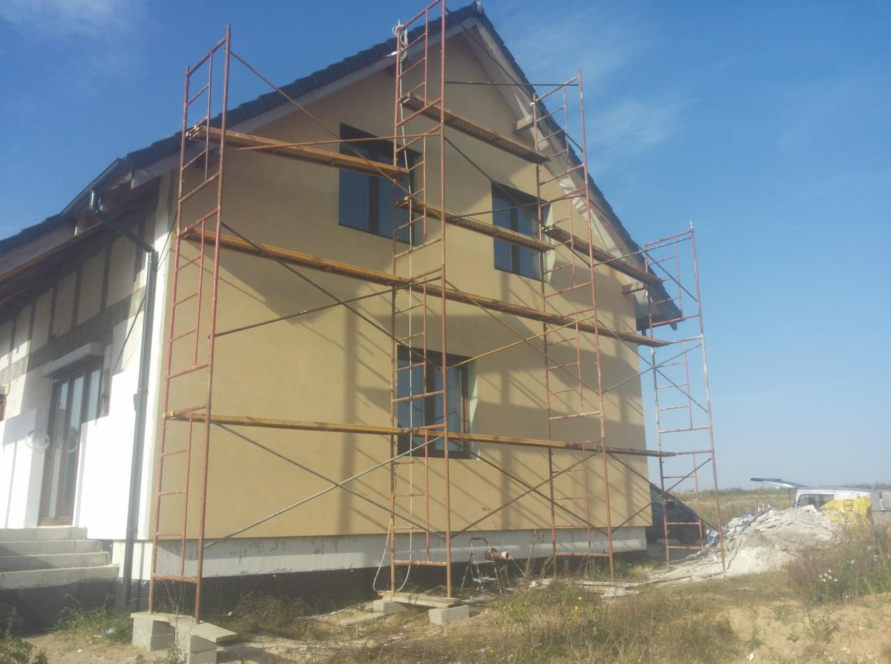 Dom murowany w trakcie szpachlowania elewacji, widoczne rusztowania i fragmenty nieotynkowanej ściany bocznej.