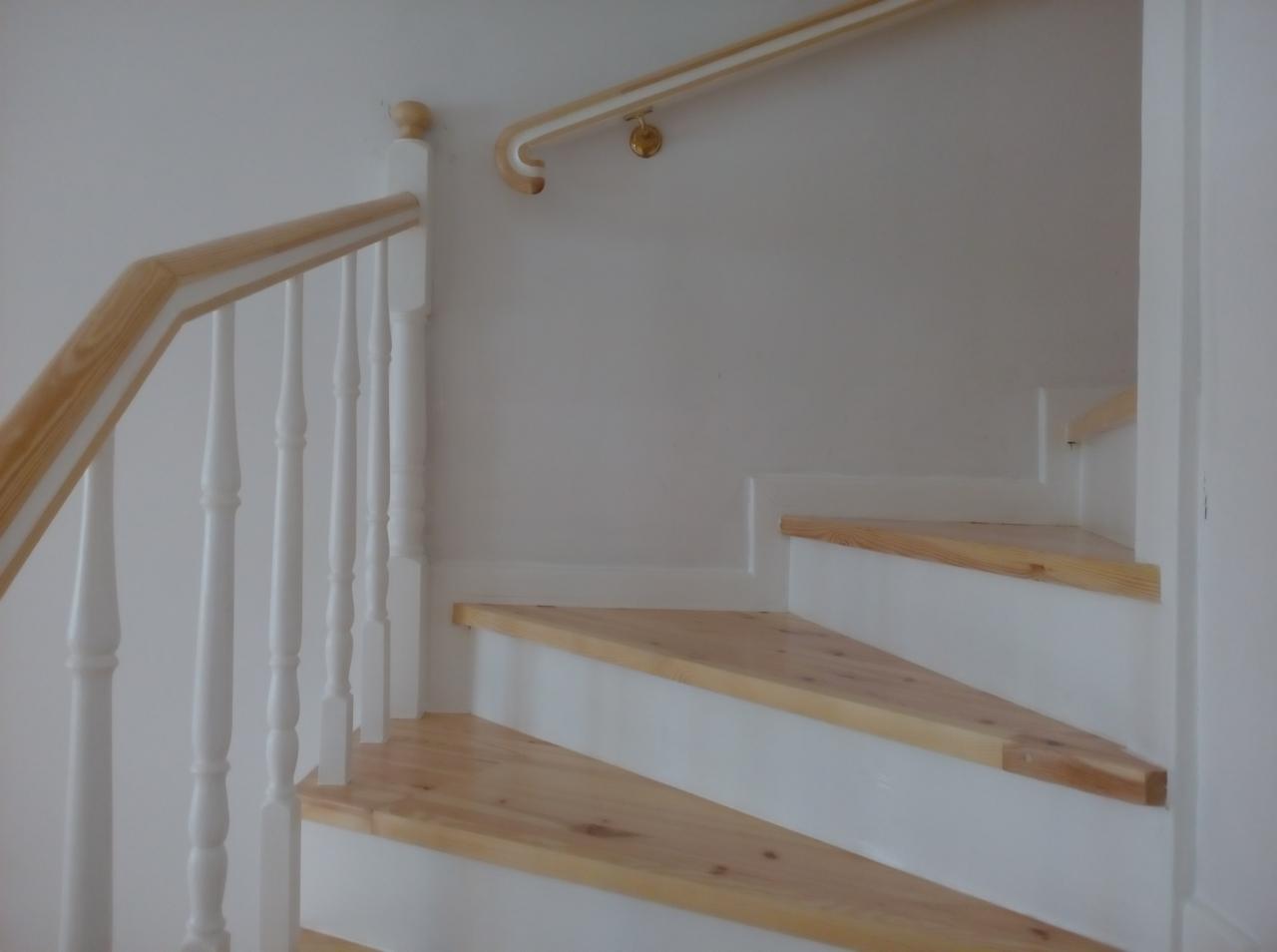 Schody drewniane z białymi podstopnicami i jasnym drewnem na stopniach oraz poręczą z jasnego drewna z białymi tralkami, widok z dołu.
