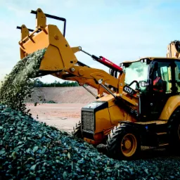 Żółta koparko-ładowarka wysypuje żwir na placu budowy w Ostrowcu Świętokrzyskim, widoczne oznaczenie modelu 432F2.