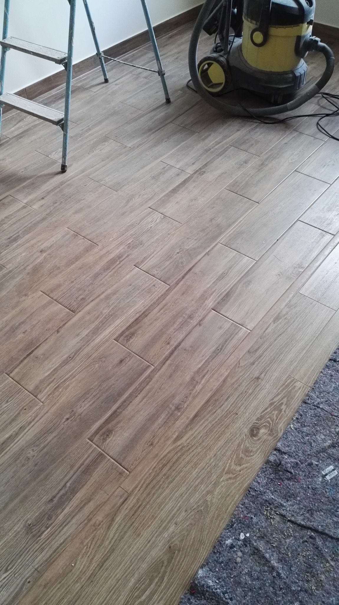 Ułożona podłoga z paneli imitujących drewno w Brodowie, widoczna drabina malarska i odkurzacz przemysłowy.