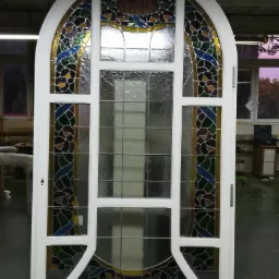 Białe, łukowe drzwi z witrażami w kwiatowe wzory, stojące w warsztacie z betonowym sufitem