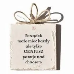 Dekoracyjny, kwadratowy kamień z napisem 'Porządek może mieć każdy ale tylko GENIUSZ panuje nad chaosem', ozdobiony sznurkową kokardą.