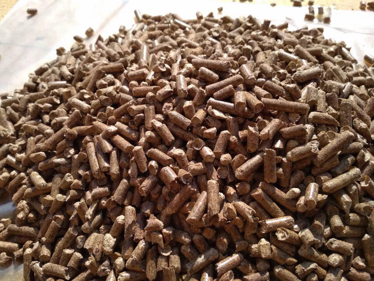 Góra brązowego pelletu drzewnego o nieregularnych kształtach i różnej długości, oświetlona z góry naturalnym światłem.