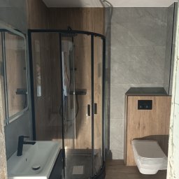 BUD-SOW - Wykończona łazienka z kabiną prysznicową, umywalką z szafką i toaletą w zabudowie. Płytki imitujące drewno i marmur. Oświetlenie punktowe.