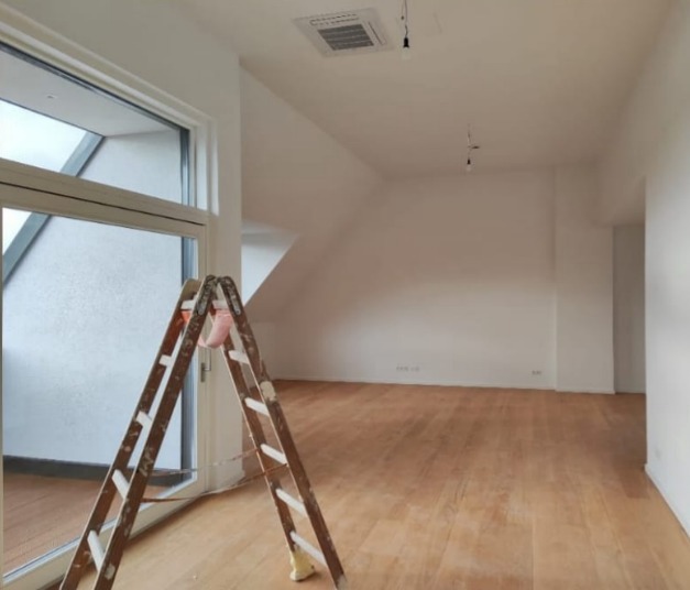 Jasne poddasze po malowaniu, z drewnianą podłogą i drabiną malarską przy oknie, widoczne detale wykończenia.