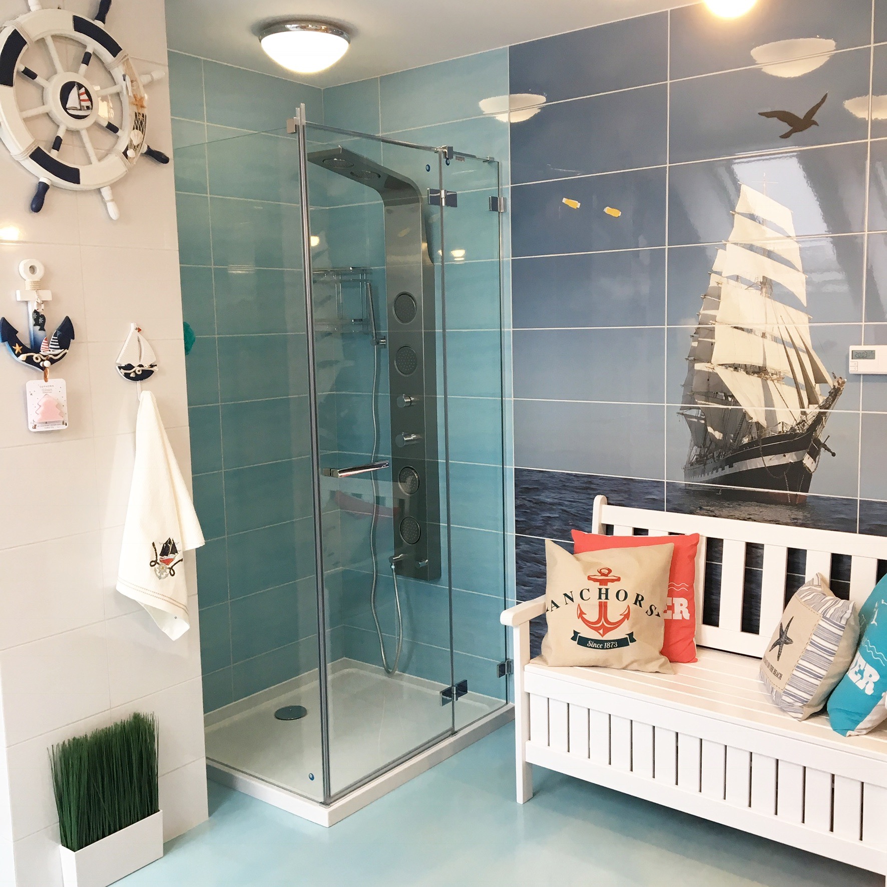 Morska aranżacja łazienki z kabiną prysznicową, dekoracjami marynistycznymi i płytkami z motywem żaglowca.