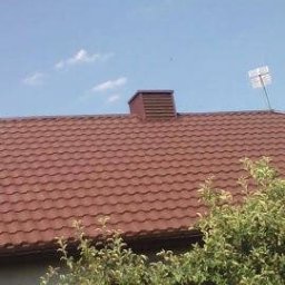 Dach-Mix - Czerwono-brązowe pokrycie dachowe z blachy trapezowej, widok z dołu, komin z brązową obudową, antena telewizyjna na dachu, błękitne niebo z chmurami w tle, częściowo zasłonięte przez gałęzie drzew.