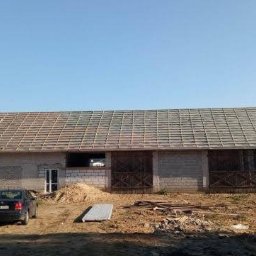 Dach-Mix - Budynek gospodarczy z częściowo zdjętym dachem, widoczna konstrukcja łatowania pod nowe pokrycie, na podwórzu zaparkowany samochód i składowane płyty.