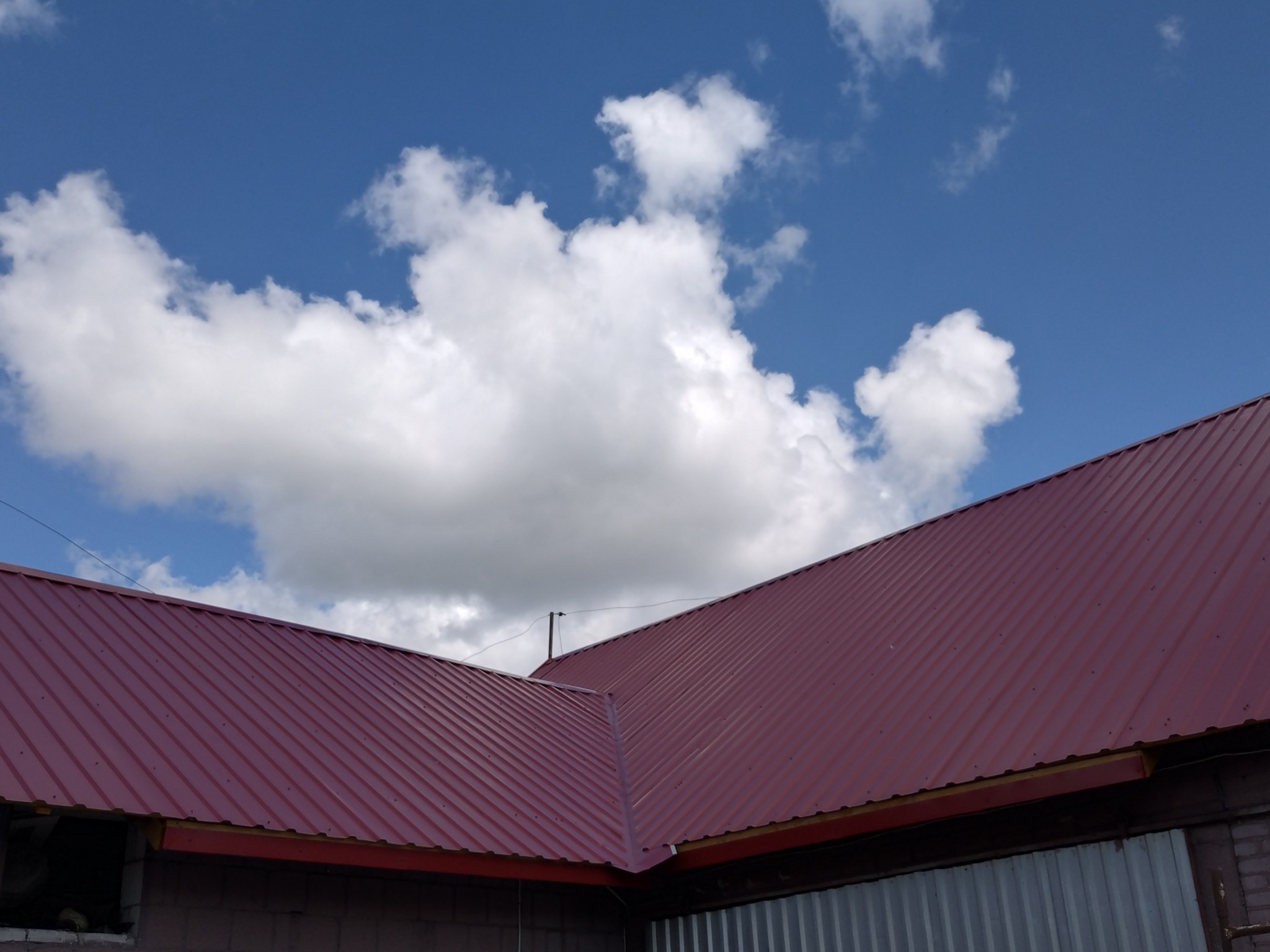 Czerwony dach z blachy trapezowej, widok z dołu na tle błękitnego nieba z białymi chmurami.