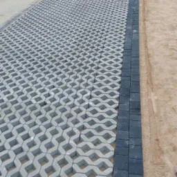 Szare ażurowe płyty ułożone na piasku, obrzeże z ciemnoszarych kostek.