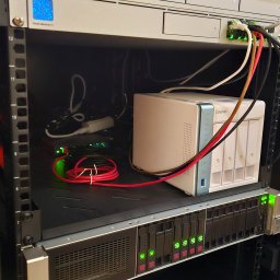 Proste IT Sp. z o.o. - Serwerownia z urządzeniami sieciowymi: NAS QNAP, przełącznik, router. Widoczne kable i diody sygnalizacyjne. Sprzęt zamontowany w szafie rack.