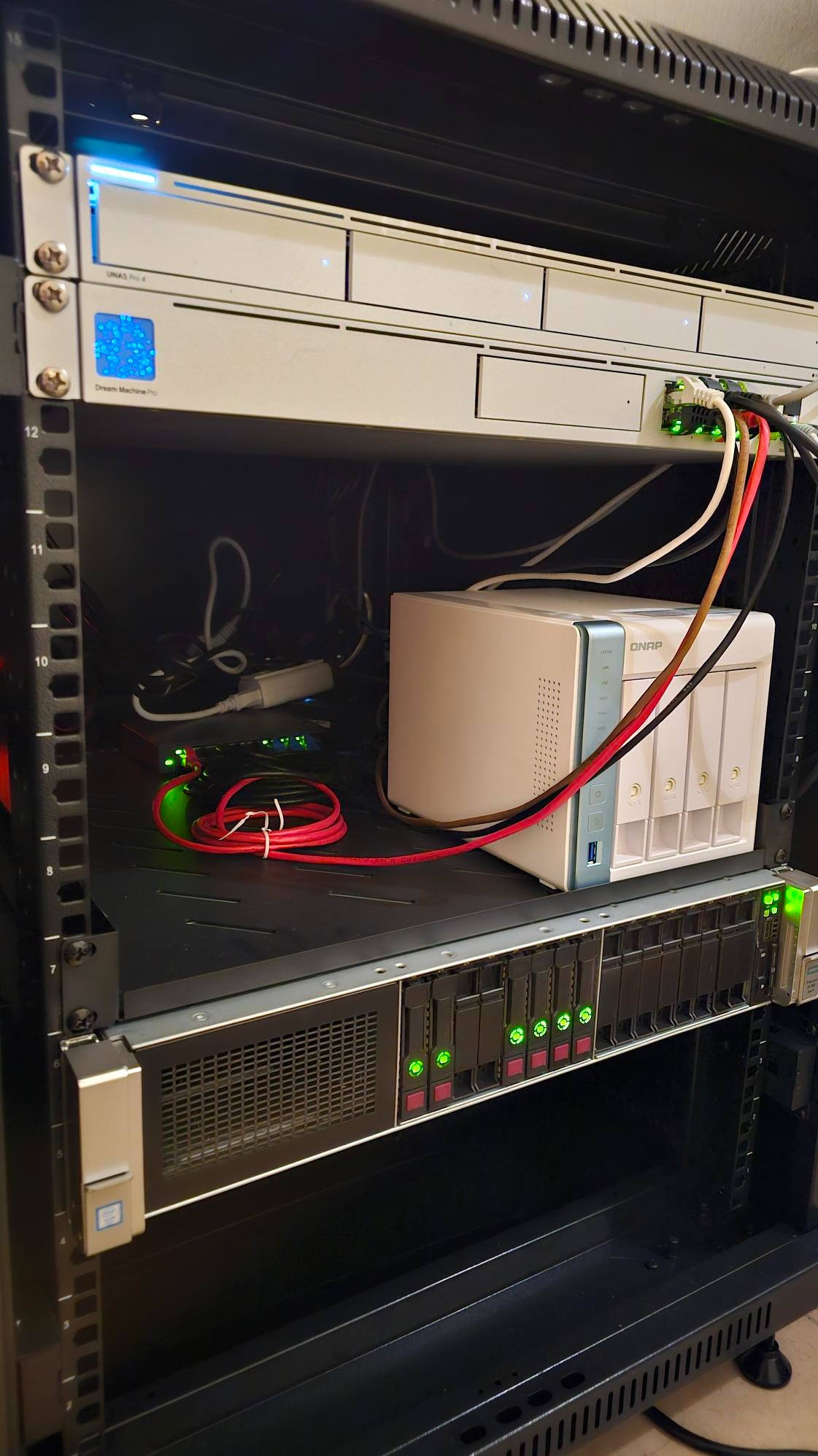 Serwerownia z urządzeniami sieciowymi: NAS QNAP, przełącznik, router. Widoczne kable i diody sygnalizacyjne. Sprzęt zamontowany w szafie rack.