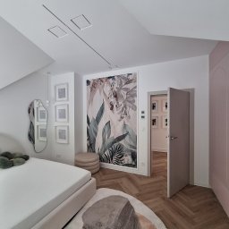 Tech-mal.pl - Nowoczesna sypialnia w jasnych barwach z fototapetą w motywy roślinne, designerskim lustrem i otwartymi drzwiami do kolejnego pomieszczenia.