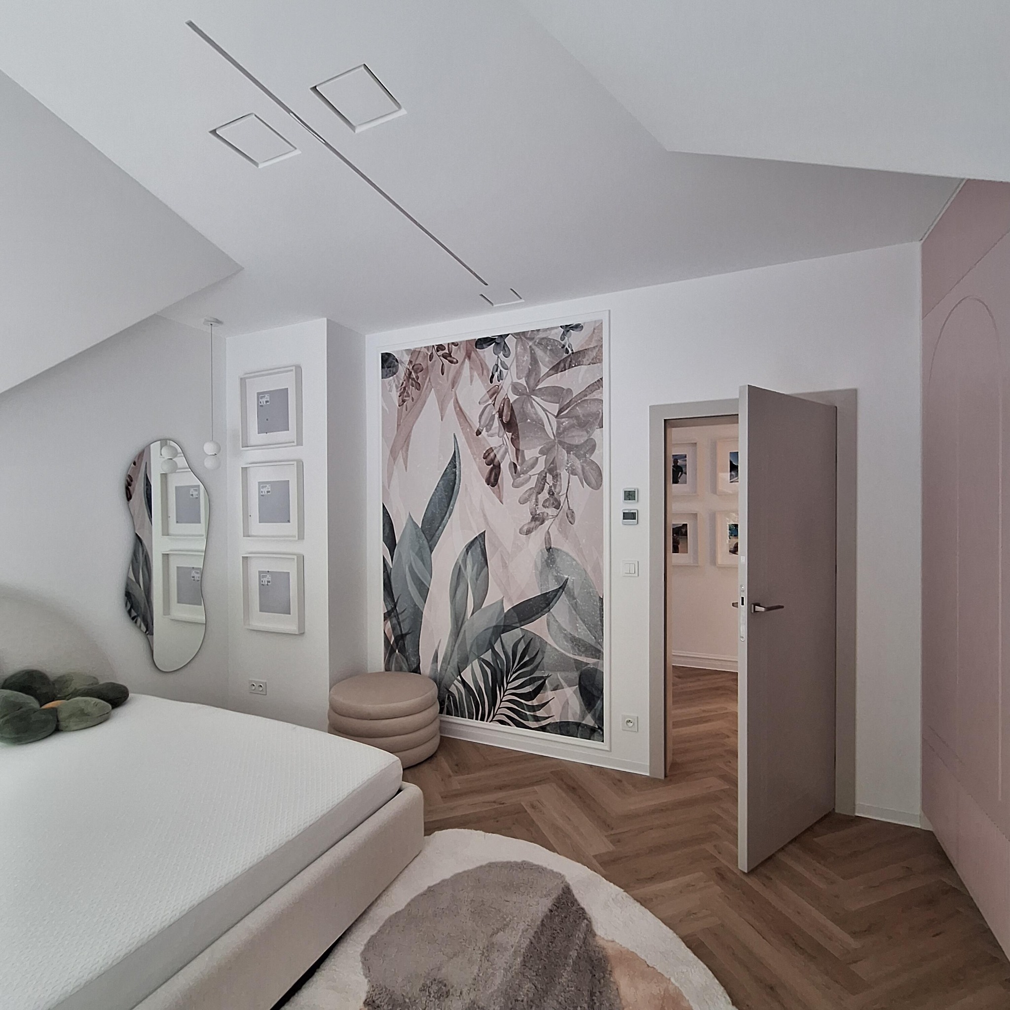 Nowoczesna sypialnia w jasnych barwach z fototapetą w motywy roślinne, designerskim lustrem i otwartymi drzwiami do kolejnego pomieszczenia.