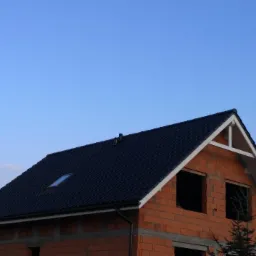 Nowy, ciemny dach z oknem połaciowym na domu w stanie surowym w Gorzycach, z widocznymi pustakami ceramicznymi i białym wykończeniem szczytu.