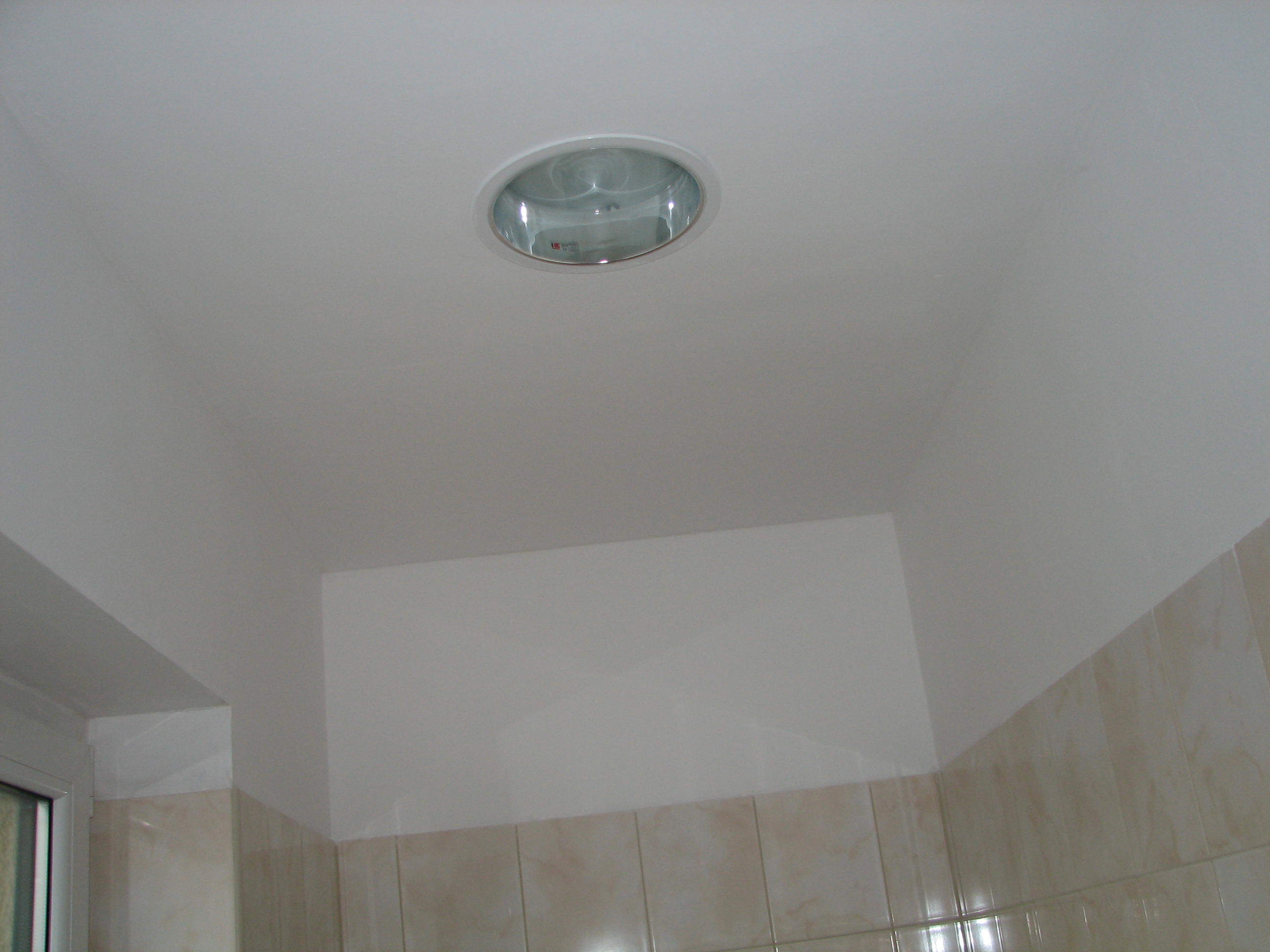 Świeżo otynkowany, biały sufit z zamontowanym okrągłym halogenem w pomieszczeniu z beżowymi płytkami ściennymi