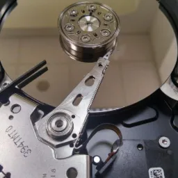 Wnętrze dysku twardego z widoczną głowicą i talerzem, z bliska, ukazujące precyzyjną mechanikę.