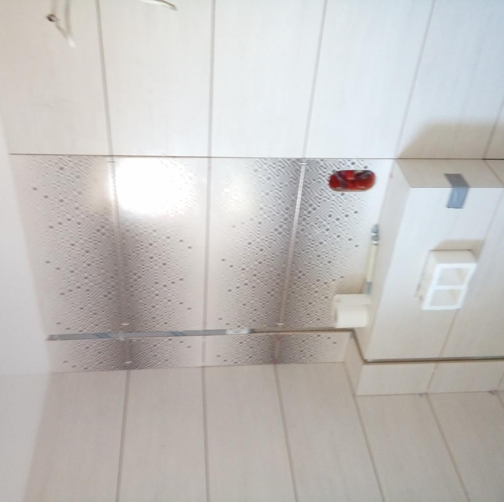 Wykończona łazienka z białymi płytkami imitującymi drewno na ścianach i podłodze, oraz panelem dekoracyjnym z geometrycznym wzorem pod sufitem, widoczny fragment toalety podwieszanej z szarą taśmą.