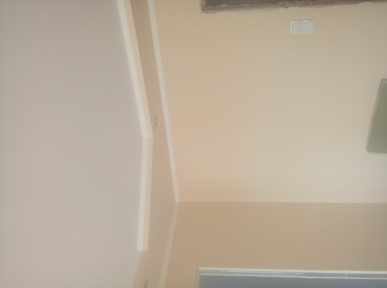 Pomieszczenie po malowaniu ścian i sufitu na jasny beż, widoczne listwy przypodłogowe i gniazdko elektryczne.