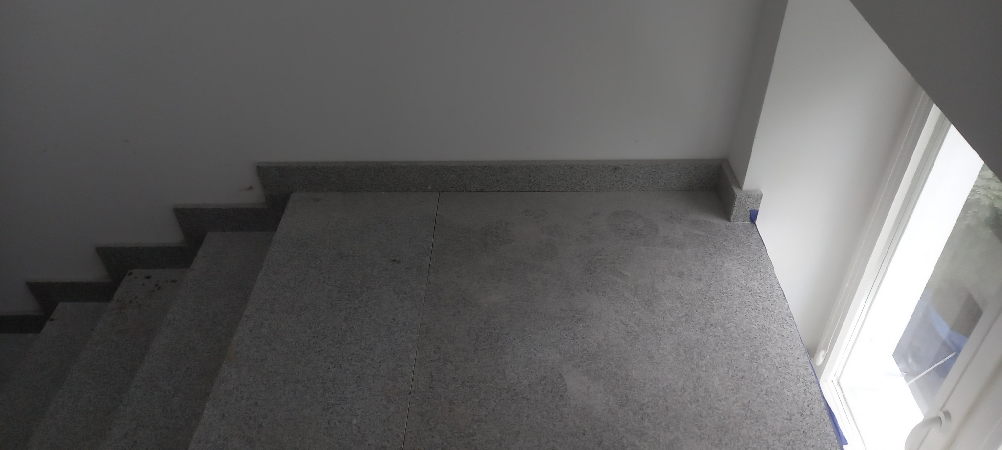 Szare schody wewnętrzne z kamienia, widok z góry, zabezpieczone niebieską taśmą malarską przy ścianie i oknie.