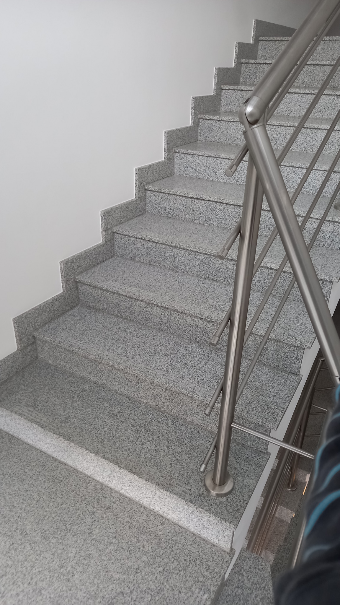 Schody wewnętrzne z szarego lastryko, wykończone metalową balustradą ze stali nierdzewnej, widok z góry.