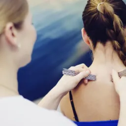 Akupunktura w Wejherowie: Terapeutka używa metalowych narzędzi do stymulacji punktów akupunkturowych na plecach pacjentki.