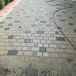 Chodnik z kostki brukowej ułożonej we wzór z szarymi akcentami, część powierzchni jest jeszcze brudna, a wąż ciśnieniowy leży na czystej części.