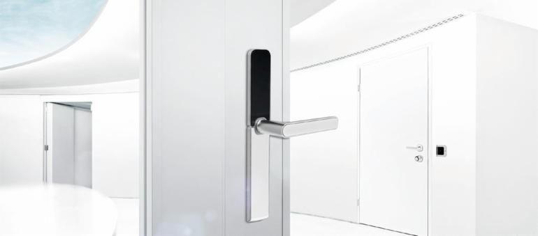 Minimalistyczne, białe wnętrze z otwartymi drzwiami z elektronicznym zamkiem i chromowaną klamką, widok na kolejne pomieszczenie z identycznymi drzwiami.
