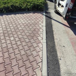 OL-KOP Usługi Koparką Mariusz Olczyk - Częściowo ułożona, czerwona kostka brukowa w kształcie litery H, oddzielona krawężnikiem od świeżo wylanego asfaltu, obok zaparkowany biały samochód dostawczy z otwartymi drzwiami.