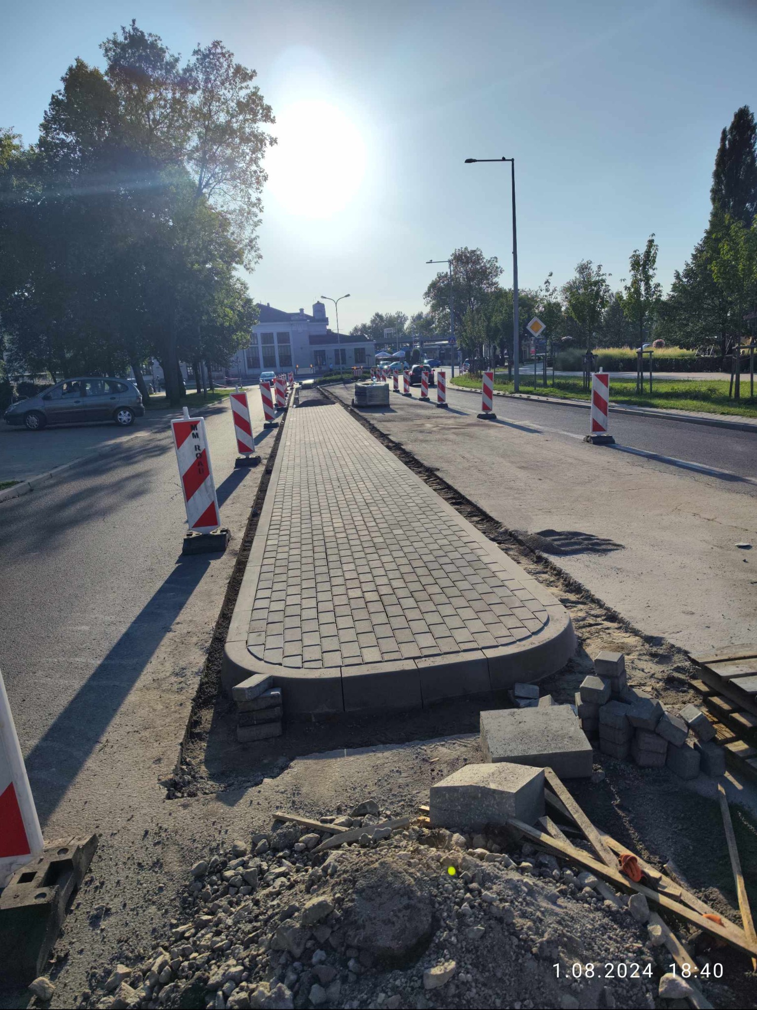 Fragment nowej ścieżki z kostki brukowej w Koninie, oddzielonej od jezdni barierkami, w trakcie prac wykończeniowych.