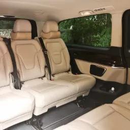 Wnętrze luksusowego busa z beżowymi skórzanymi fotelami, widok z tyłu kabiny pasażerskiej, butelka wody w uchwycie.